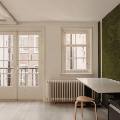 Kantoorruimte huren aan de Prins Hendrikkade 14 in Amsterdam Centrum, met uitzicht op aangrenzende gebouwen, voorzien van een tafel en stoelen, geschikt als werkruimte.