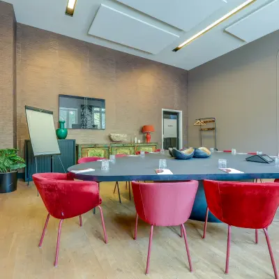 Stijlvolle vergaderruimte in het kantoorpand op Raamplein 1, Amsterdam Centrum, met een grote ovale tafel en moderne rode stoelen. Ideaal voor wie kantoorruimte wil huren.