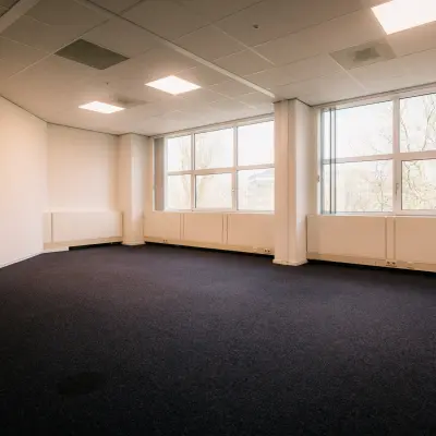 Ruime kantoorkamer op Overschiestraat 182, Amsterdam De Schinkel voor kantoorruimte huren. Grote ramen zorgen voor natuurlijk licht op de blauwe vloeren, ideaal voor een flexibel indeelbare werkruimte.