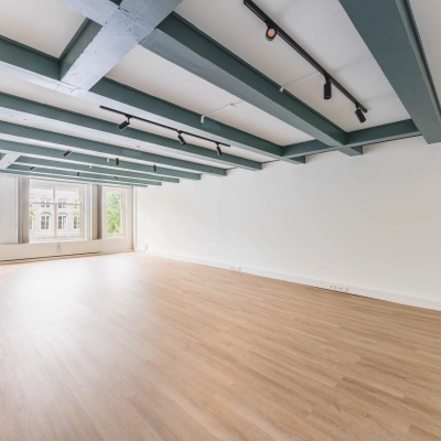 Leeg kantoorpand aan Herengracht 221, Amsterdam Grachtengordel, met houten vloer en balkenplafond, zicht op groene omgeving door grote ramen. Optimaal voor kantoorruimte huren.