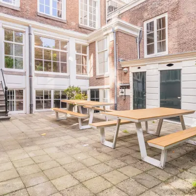 Binnenplaats van een kantoorpand aan de Herengracht 582-584 in Amsterdam Grachtengordel, met houten picknicktafels op een betegeld terras omgeven door stenen muren.