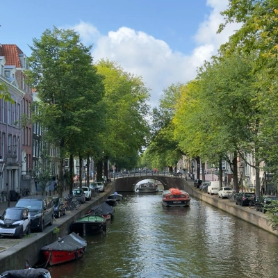 Uitzicht op de Amsterdamse gracht met boten, omringd door groene bomen langs Herengracht. Geen personen zichtbaar. Ideale locatie voor een kantoorruimte huren met authentieke charme.