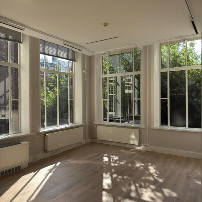 Lichte kantoorruimte te huur met grote ramen aan de Herengracht 582-584, Amsterdam Grachtengordel, zonder meubilair, met uitzicht op de binnentuin en houten vloeren.