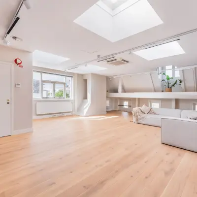 Moderne en lichte kantoorruimte te huur aan de Herengracht 582-584, Amsterdam Grachtengordel, met een houten vloer, comfortabele bank en planten, geschikt voor diverse doeleinden.