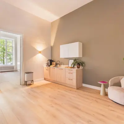 Een lichte en uitnodigende kantoorruimte met houten vloer, een kitchenette, en comfortabele zitgelegenheid aan de Herengracht in Amsterdam, ideaal om te huren als kantoorpand.