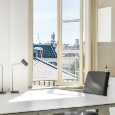Licht kantoorpand op Keizersgracht 261 in Amsterdam Grachtengordel met een modern bureau en stoelen, uitzicht op daken door grote ramen. Ideale plek voor kantoorruimte huren.
