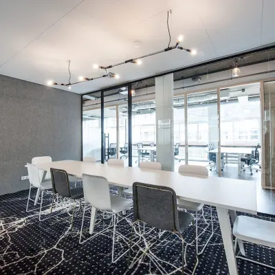 Moderne kantoorruimte met lange witte tafel en acht stoelen op Singel 542, Amsterdam Grachtengordel. Veel lichtinval door grote ramen, ideaal voor vergaderingen. Achterin zicht op open kantoorruimtes voor huur.