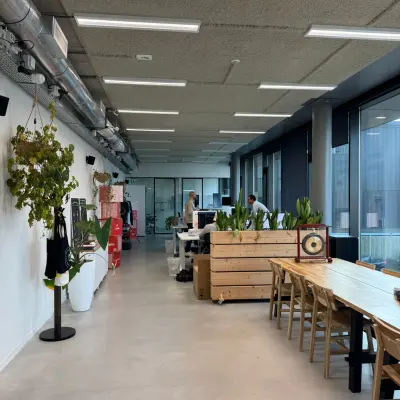 Kantoorruimte huren aan de Moermanskkade 303 in Amsterdam Houthavens, met houten tafels, planten en zicht op lange werkplekken waar mensen werken aan bureaus.