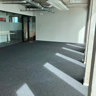 Lege kantoorruimte te huur op Overhoeksplein 1 in Amsterdam Noord met grijze vloerbedekking en glazen wanden.