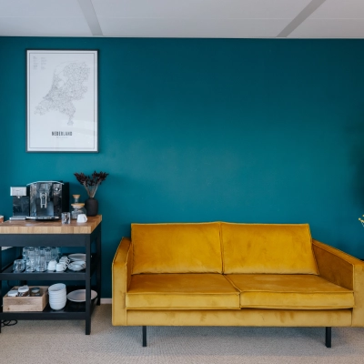 Lichte kantoorruimte in Amsterdam Noord met een gele bank, een koffietafel en een diepblauwe muur. Ideale plek om kantoorruimte te huren.