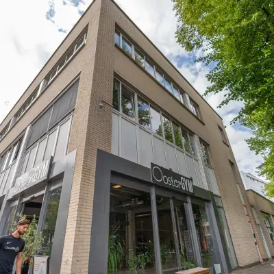 Het kantoorpand op James Wattstraat 71 in Amsterdam Oost toont een moderne gevel met grote ramen en groene beplanting aan de buitenzijde.