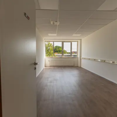 Lege kantoorruimte met houten vloer en groot raam in het kantoorpand op James Wattstraat 71, Amsterdam Oost. Ideaal om te huren voor een persoonlijk touch en inrichting naar eigen wens.