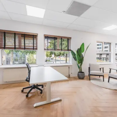 Verlichte kantoorruimte te huur aan de Arlandaweg 92, Amsterdam Sloterdijk met houten vloer, groot bureau en vensterplanten. Ideaal voor werk of vergaderingen met uitzicht op de stad.