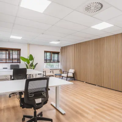 Lichte kantoorruimte huren op Arlandaweg 92, Amsterdam Sloterdijk. Het kantoorpand heeft een moderne houten wand en houten vloer, met verstelbare bureaus en stoelen, ideaal voor creatieve werkplekken.