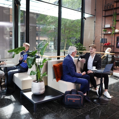 Moderne kantoorruimte aan de Teleportboulevard 110 in Amsterdam Sloterdijk met mensen die vergaderen en koffie drinken tussen planten en stijlvol meubilair.