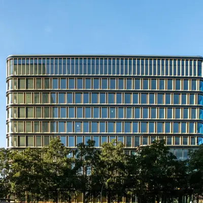 Modern kantoorpand aan het Kon. Wilhelminaplein 4 in Amsterdam West met glazen gevel en omliggende bomen, ideaal voor kantoorruimte huren.