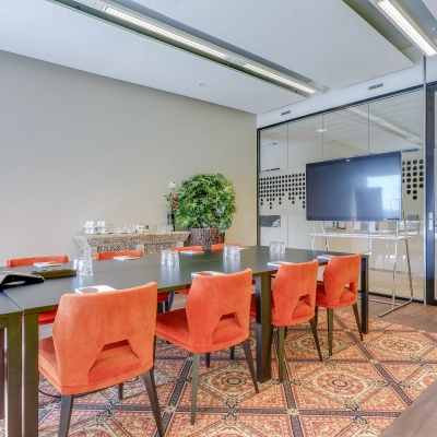 Een moderne vergaderruimte in een kantoorpand in Amsterdam Zuid-Oost, met een grote tafel, rode stoelen en een groot scherm. Een ideale plek voor zakelijke bijeenkomsten of kantoorruimte huren.