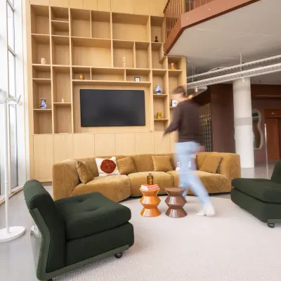 Moderne, gemeubileerde lounge in een kantoorpand aan Luttenbergweg 8, Amsterdam Zuid-Oost, met comfortabele zitplaatsen en een wandmeubel. Een persoon loopt door de ruimte.