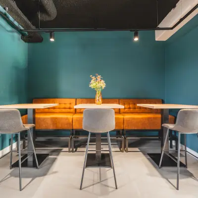 Kantoorruimte te huur in Amsterdam Zuid-Oost met een zithoek voorzien van moderne tafels, stoelen en een oranje bank tegen een turquoise muur op Paasheuvelweg 20.