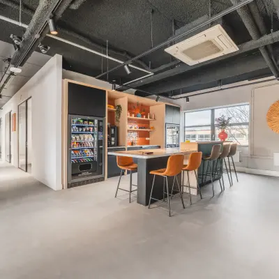 Moderne kantoorruimte op Paasheuvelweg 20, Amsterdam Zuid-Oost met een gemeubileerd interieur, voorzien van hoge tafels en een verkoopautomaat voor snacks en drankjes, ideaal voor wie een kantoorruimte wil huren.