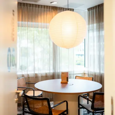 Gezellige kantoorruimte huren op Barbara Strozzilaan 101 in Amsterdam Zuidas, met een ronde tafel en moderne stoelen onder een grote, hangende lamp.