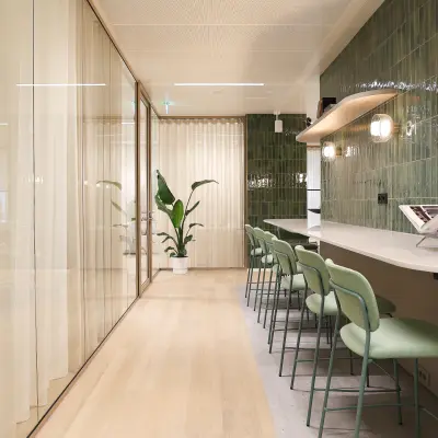 Moderne kantoorruimte te huur aan de Beethovenstraat 503 in Amsterdam Zuidas met groene tegels, hoge stoelen en glazen wanden voor een stijlvolle werkomgeving.