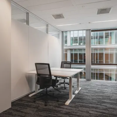Moderne kantoorruimte huren op Claude Debussylaan 10, Amsterdam Zuidas, met twee bureaus en stoelen, omgeven door grote ramen voor natuurlijk licht.