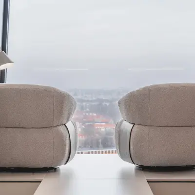 Moderne kantoorruimte met twee comfortabel ogende fauteuils en grote ramen met uitzicht over Amsterdam. Ideaal voor ontspannen vergaderingen of creatieve brainstormsessies in de Zuidas.
