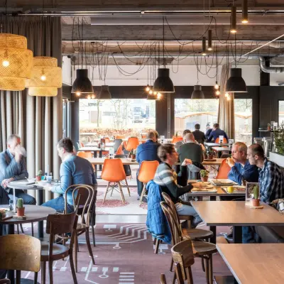 Lichte en moderne werkruimte met zitplaatsen voor zakelijke bijeenkomsten in kantoorpand op Oude Apeldoornseweg 41-45, Apeldoorn. De ruimte is gemeubileerd en mensen voeren zakelijke activiteiten uit.