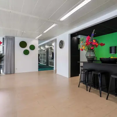 Kantoorruimte in Apeldoorn op Prins Willem-Alexanderlaan 301 met moderne inrichting, inclusief kleurrijke bloemen, enkele krukken en een open vloerplan voor kantoor activiteiten. Ideaal voor huren.