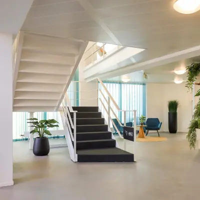 Moderne kantoorruimte huren in Apeldoorn met stijlvolle inrichting, inclusief open trap, planten en zitgedeelte. Lichte ruimte geschikt voor ontvangst en ontspanning.
