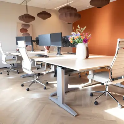 Moderne kantoorpand met houten vloer, werkplekken met bureaustoelen en schermen op Schumanpark 9, Apeldoorn. De ruimte is licht en uitnodigend voor kantoorruimte huren.