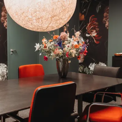 Stijlvolle kantoorruimte huren in Arnhem IJsseloord aan Vlamoven 34 met moderne vergadertafel, felgekleurde stoelen en decoratieve bloemenvaas.