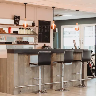 Moderne kantoorruimte met een stijlvolle bar met hoge stoelen en sfeervolle verlichting, ideaal voor informeel overleg en ontspanning. Perfect om een kantoorruimte te huren op Vlamoven 34 in Arnhem IJsseloord.