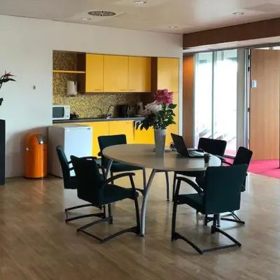 Foto van een gemeubileerd kantoor in Arnhem-Zuid met ronde tafel en stoelen, ideaal voor een kort overleg. Geel keukentje op de achtergrond. Kantoorruimte huren biedt praktische werkplekken.