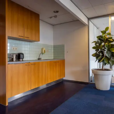 Kantoorruimte huren op Kronenburgsingel 525 in Arnhem Zuid, met een kleine kitchenette en een grote plant naast een glazen wand.