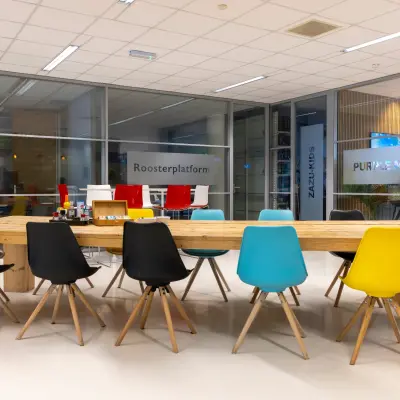 Vergaderruimte in een modern kantoorpand op de Amalialaan 126, Baarn. Verschillende gekleurde stoelen rondom een houten tafel. Glaswanden scheiden ruimtes.