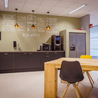 Moderne pantry in kantoorpand met een houten tafel, kleurrijke stoelen en keukenapparatuur op Amalialaan 126, Baarn.