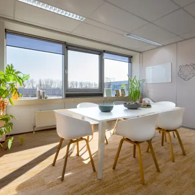 Lichte kantoorruimte op Kamerlingh Onnesweg 10, Barendrecht, met een witte tafel en stoelen, omringd door ramen en planten.