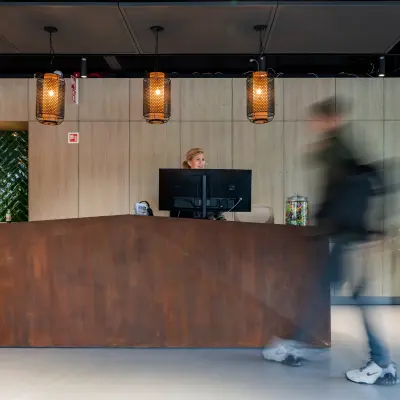 Moderne receptie in kantoorpand aan de Baron van Nagellstraat 136, Barneveld met houten balie, groen tegelwerk en planten. Persoon staat achter de balie en verwelkomt bezoekers in de kantoorruimte.