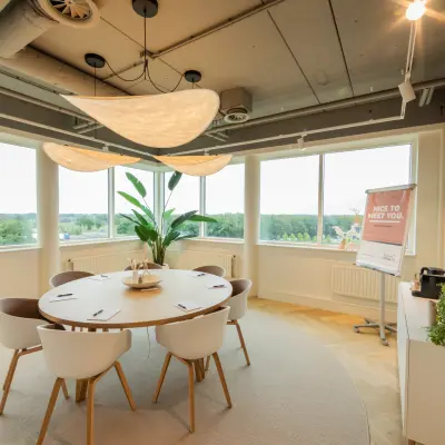 Moderne, lichte kantoorruimte met ronde tafel en stoelen, geschikt voor vergaderingen. De grote ramen bieden uitzicht op groen landschap. Perfect om een kantoorruimte te huren in Barneveld.