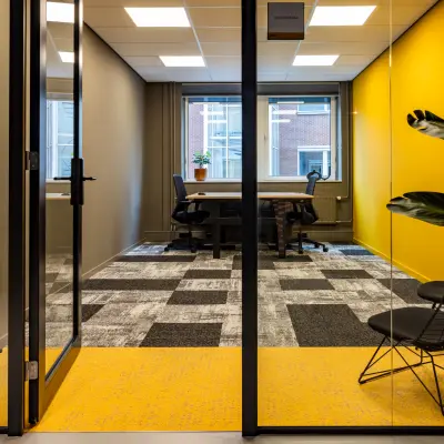 Moderne kantoorruimte te huur op Baron van Nagellstraat 136 in Barneveld met glazen wanden, opvallende gele details en stijlvolle zwarte stoelen.