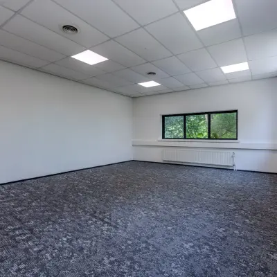 Lege kantoorruimte met grijs tapijt en rechthoekig raam in kantoorpand aan de Rijtuigweg 10, Bergen op Zoom, klaar voor huur.