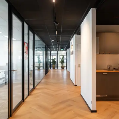 Verlichte gang in kantoorpand Tolnasingel 1-3, Bodegraven, met glazen wanden en een moderne pantry aan de rechterkant. Kantoorruimte huren hier biedt stijlvol ingerichte werkruimtes en faciliteiten.