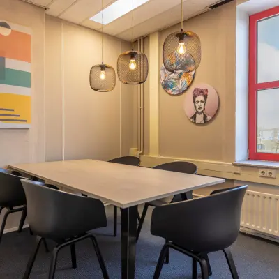 Stijlvolle kantoorruimte huren in Breda Oost-Brabantpark met moderne kunst aan de muur, grote tafel en stoelen onder sfeervolle lichten.