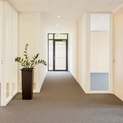 Heldere gang in kantoorpand Druivenstraat 25-31 in Breda Oost, met deuren naar verschillende kantoorruimtes. Planten dragen bij aan een frisse uitstraling. Ideaal voor het huren van kantoorruimte.