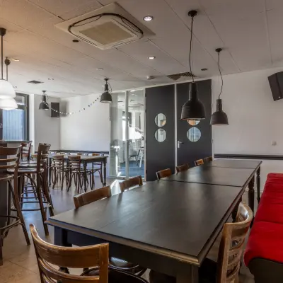 Een moderne kantoorruimte op Druivenstraat 25-31 in Breda Oost met houten tafels en stoelen, rode bank en decoratieve lampen. Geschikt voor huur, het kantoorpand biedt een veelzijdige omgeving voor werk.