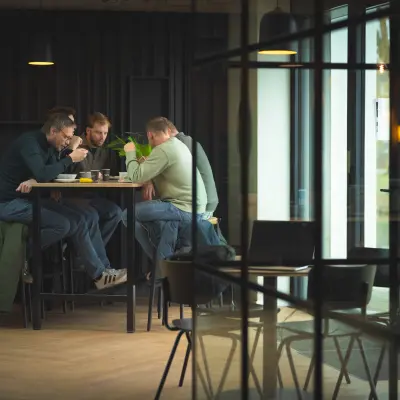 Zakelijke bijeenkomst in een moderne kantoorruimte op Rietbaan 2-12, Capelle aan den IJssel. Drie personen aan een hoge tafel in een gemeubileerde ruimte met veel lichtinval.