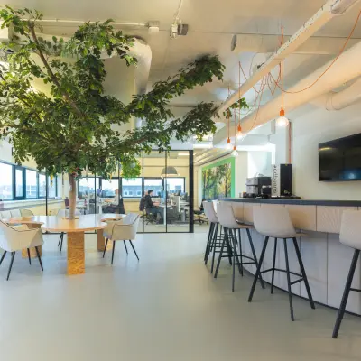 Moderne kantoorruimte op Rietbaan 2-12 in Capelle aan den IJssel, met een grote plant, stijlvolle zithoek en bar met krukken. Perfect om te huren voor zakelijke bijeenkomsten.
