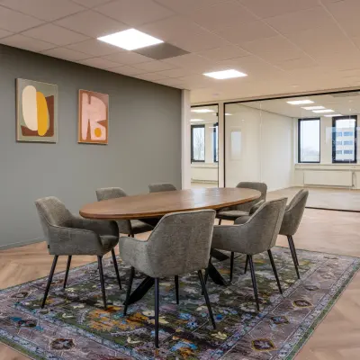 Moderne kantoorruimte met houten vergadertafel en zes stoelen op een kleurrijk tapijt, gelegen aan Vlierbaan 20, Capelle aan den IJssel. Ideale plek om kantoorruimte te huren voor zakelijke bijeenkomsten.